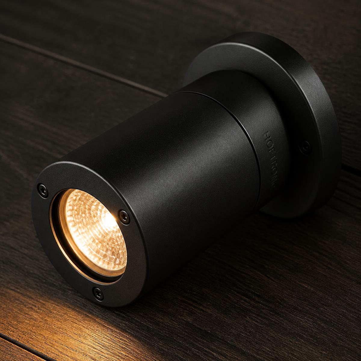 Black aluminium outdoor lighting fixture casting a warm beam across dark wood